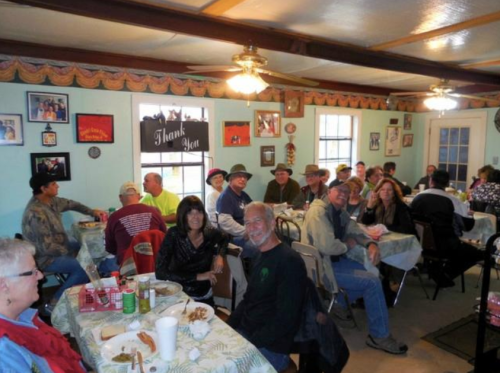 A group of people enjoying a meal together in a cozy dining room, with decorations and a "Thank You" sign on the wall.