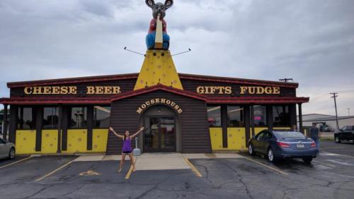A woman stands in front of a quirky store called "Mousehouse," featuring a large mouse statue and colorful signage.