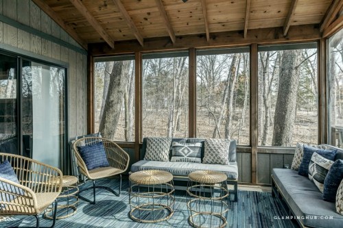 Cozy screened-in porch with wooden ceiling, stylish seating, and views of trees outside.