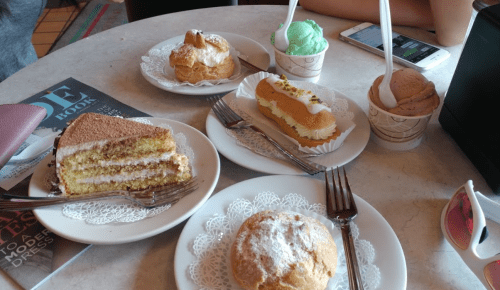 A table with various desserts: cake, pastries, and ice cream in cups, with forks and napkins.