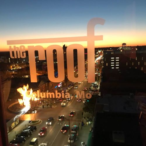View of a city street at sunset, with "the roof" sign prominently displayed in the foreground.
