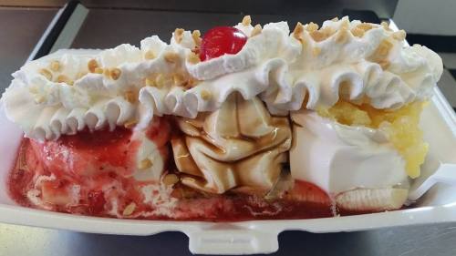 A delicious ice cream sundae with three flavors, whipped cream, nuts, and a cherry on top, served in a white dish.