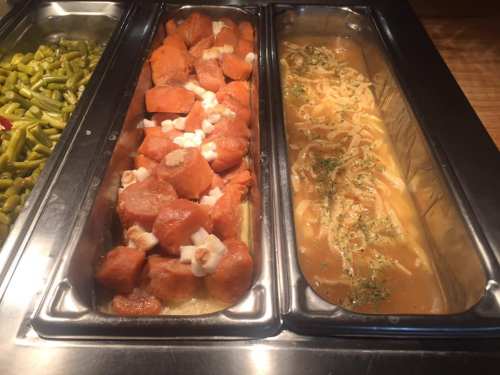 Two buffet trays: one with sweet potatoes topped with marshmallows, the other with noodles in a savory sauce.