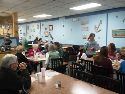 A cozy restaurant interior with diners at tables, chatting and enjoying meals, decorated with nautical-themed artwork.