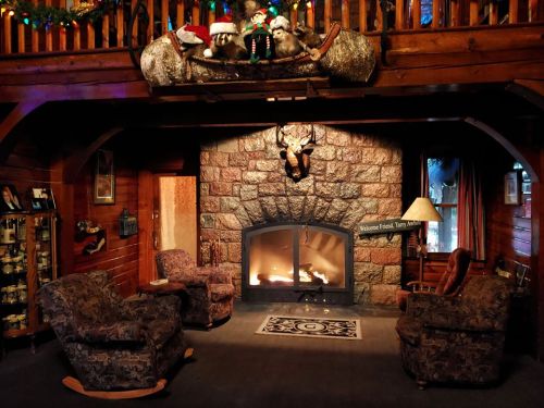 Cozy cabin interior with a stone fireplace, two armchairs, and festive decorations above, creating a warm atmosphere.
