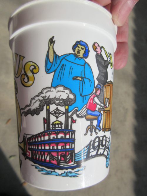 A decorative cup featuring illustrations of a steamboat, a blue-robed figure, and a person at a desk.