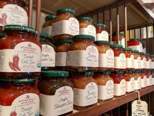 A shelf filled with various jars of jams and jellies from Stonewall Kitchen, including sweet chili and bacon flavors.
