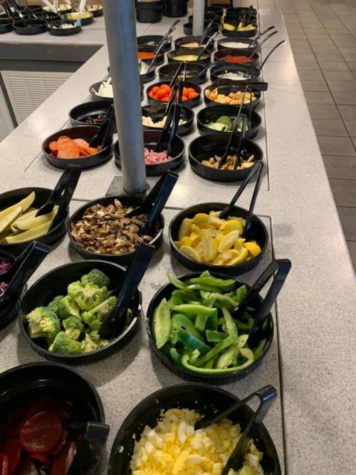 A variety of fresh vegetables and toppings in black bowls on a countertop, ready for a salad bar.