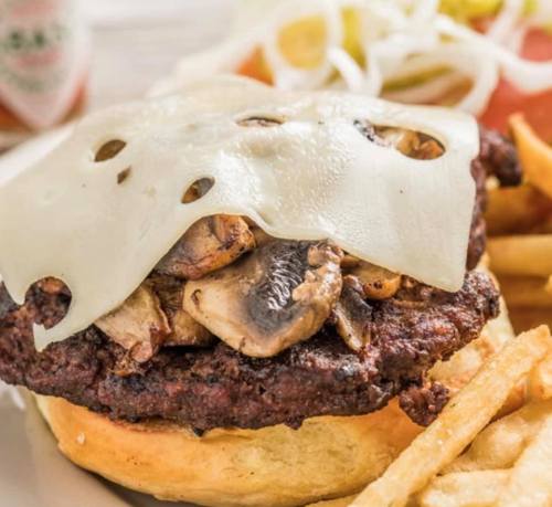 A juicy burger topped with melted cheese and sautéed mushrooms, served with fries and a side of fresh vegetables.