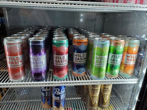 A refrigerator shelf filled with various flavors of Wild Basin sparkling water cans, arranged neatly.