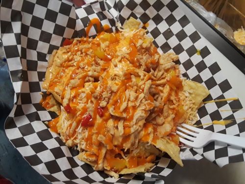 A plate of nachos topped with shredded chicken, cheese, and drizzled with sauce, served in a checkered paper basket.