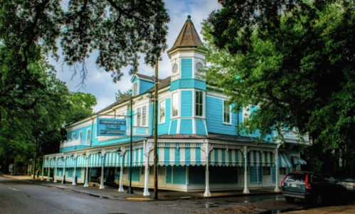 A blue Victorian-style building with a tower, surrounded by trees and featuring striped awnings.