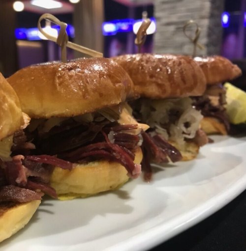 A close-up of a platter featuring several sliders with various fillings, garnished with toothpicks.