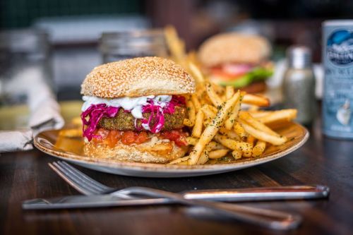 A sesame seed burger with lettuce, tomato, and purple cabbage, served with a side of seasoned fries on a wooden table.