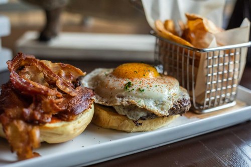 A plate featuring a burger with a fried egg, crispy bacon, and a side of fries in a small basket.
