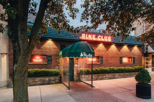 Exterior of Pine Club restaurant at dusk, featuring a green awning and glowing red neon signs.