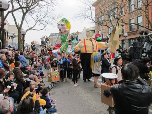 A lively parade featuring large puppets and colorful costumes, with a crowd of spectators enjoying the festivities.