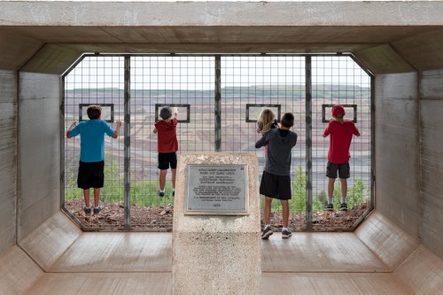 Children looking out through a viewing area at a large open pit mine, with a plaque in the foreground.