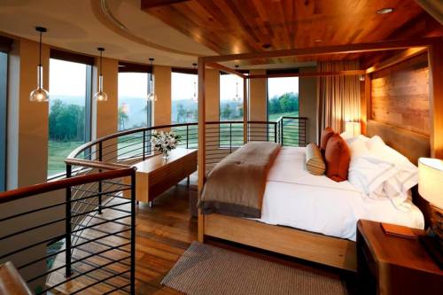 A modern bedroom with a wooden design, large windows, and a cozy bed, overlooking a scenic landscape.
