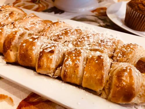 A plate of golden-brown pastry rolls dusted with powdered sugar, served on a floral tablecloth.