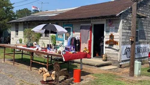A rustic shop with an open sign, featuring a table of items outside and a rocking horse on display.
