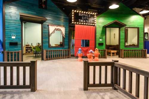 Colorful play area featuring blue and green houses, a theater stage, and playful decorations.