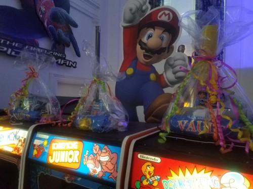 Three gift baskets with colorful ribbons sit on arcade machines, featuring classic games like Donkey Kong and Mario.