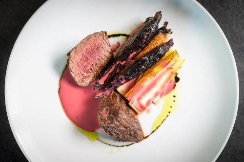A gourmet dish featuring sliced beef, charred vegetables, and colorful sauces on a white plate.