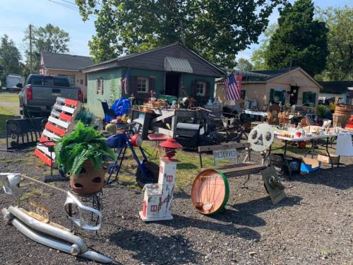 A yard filled with various antiques and collectibles, including furniture, decor, and garden items, in a sunny outdoor setting.