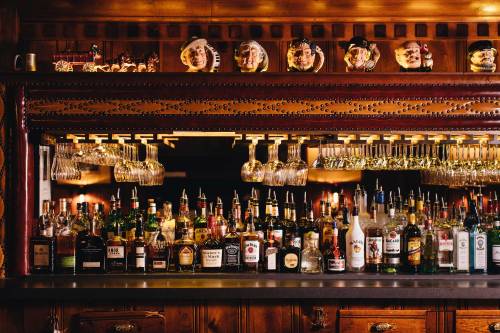 A wooden bar with a variety of liquor bottles and hanging glasses, decorated with unique wall art above.
