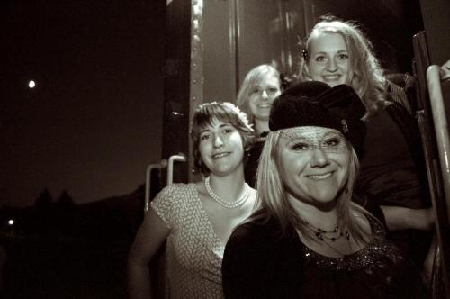 A group of four women posing together outdoors at night, smiling and dressed in stylish outfits.