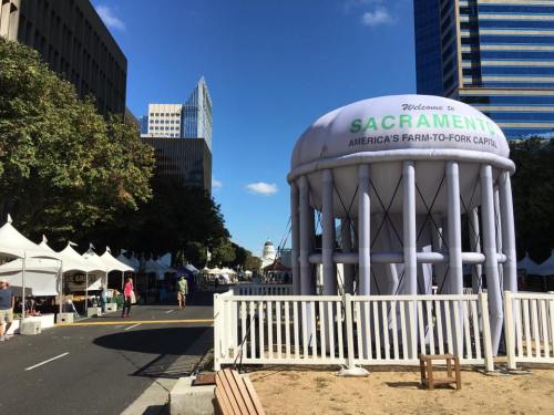 A large inflatable structure welcomes visitors to Sacramento, with tents lining the street and city buildings in the background.