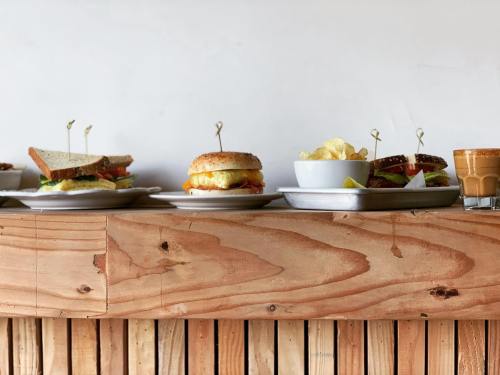 A wooden table displays various sandwiches, a bowl of chips, and a small glass of beverage.