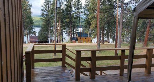 View from a wooden deck overlooking a lake surrounded by trees and cabins in a serene outdoor setting.