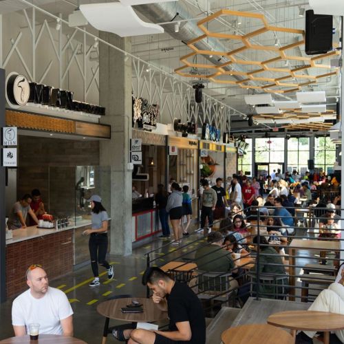 A busy café interior with people seated at tables, ordering at the counter, and a modern design featuring wooden accents.
