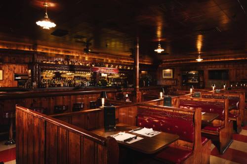 Cozy wooden interior of a bar and restaurant with red booths, dim lighting, and a well-stocked bar in the background.