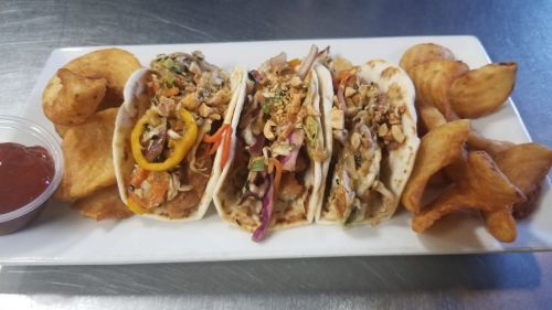 Three tacos filled with colorful ingredients, served with potato chips and a side of dipping sauce.