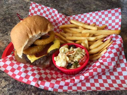 A cheeseburger with onion rings, fries, and a side of macaroni salad in a red basket with checkered paper.