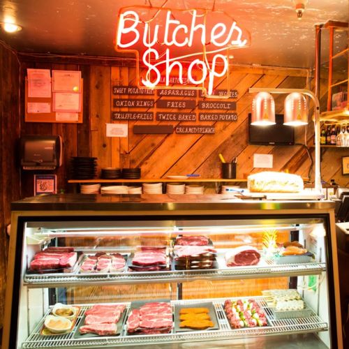 A vibrant butcher shop display with various meats and a neon sign, set against a rustic wooden backdrop.