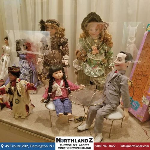 A display of vintage dolls in various outfits, including a clown and a girl in a blue dress, set in a glass case.