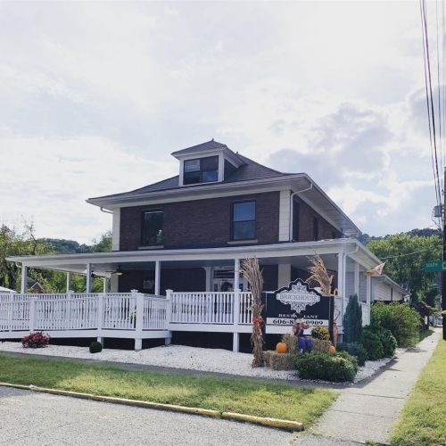 A two-story restaurant with a porch, surrounded by greenery and seasonal decorations, under a partly cloudy sky.