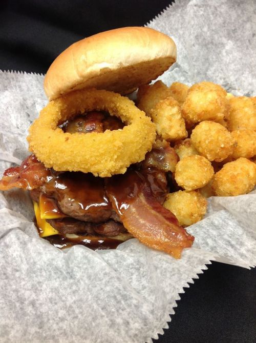 A hearty burger topped with bacon and an onion ring, served with crispy tater tots on the side.