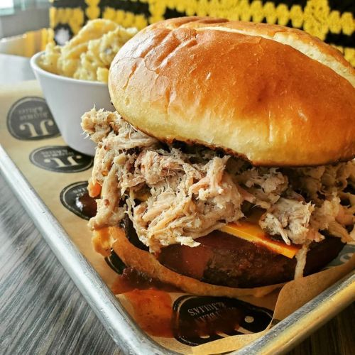 A pulled pork sandwich on a bun with cheese, served with a side of macaroni and cheese in a bowl.