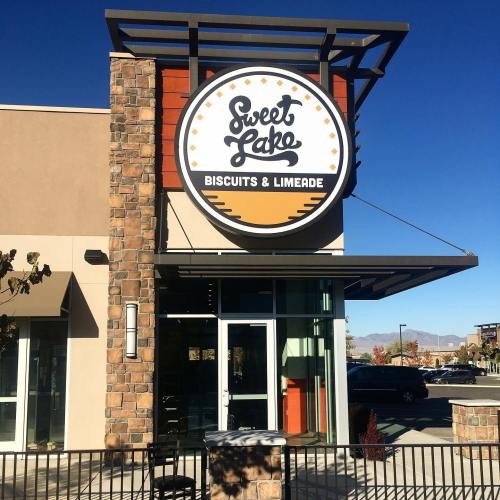 Exterior of a restaurant named "Sweet Lake Biscuits & Limeade," featuring a round sign and clear blue sky.
