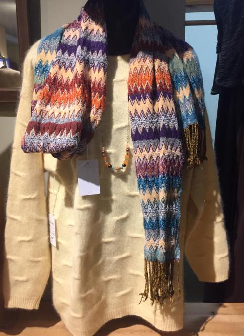 A cozy cream sweater paired with a colorful patterned scarf and a beaded necklace, displayed on a mannequin.