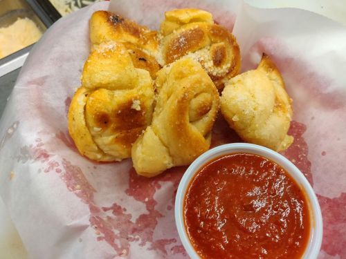 Golden, baked bread knots sprinkled with cheese, served with a side of marinara sauce in a paper-lined basket.