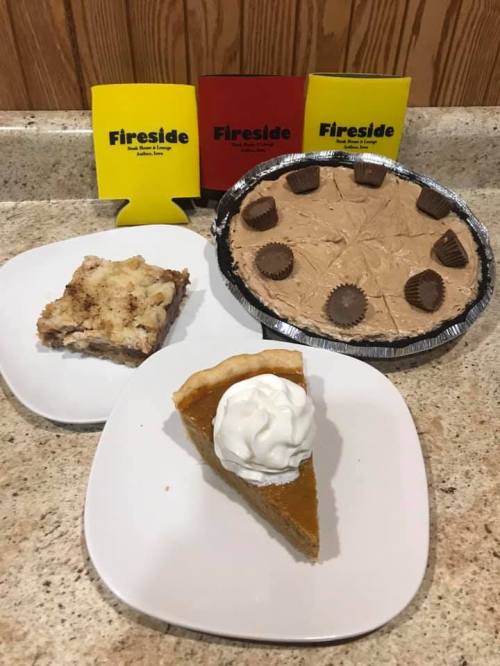 A countertop with two dessert plates: one with pumpkin pie topped with whipped cream, and another with a chocolate pie and a slice of cake.