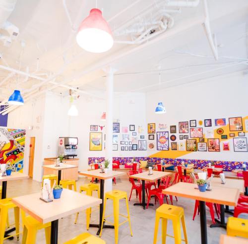 Bright, colorful restaurant interior with art-covered walls, wooden tables, and vibrant red and yellow chairs.