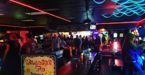 A vibrant arcade filled with people, neon lights, and classic gaming machines, creating a lively atmosphere.