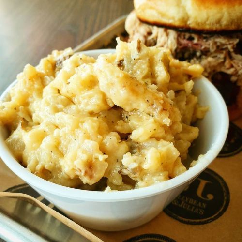 A bowl of creamy mashed potatoes served alongside a sandwich on a wooden table.